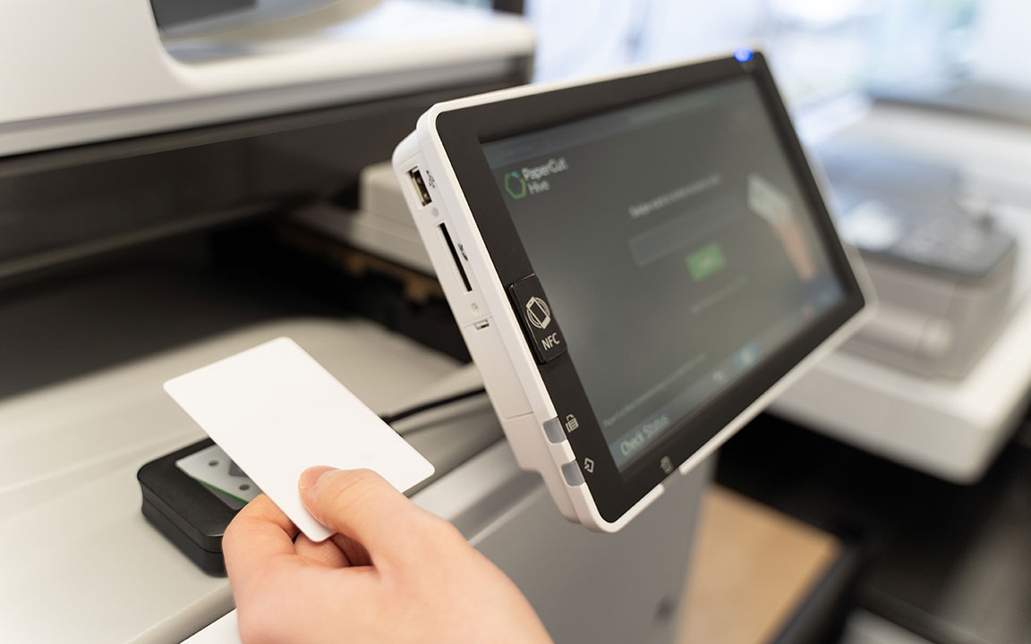  A photo of someone who is securely releasing a print document with their office access card by touching it to a card reader attaced to a printer. 